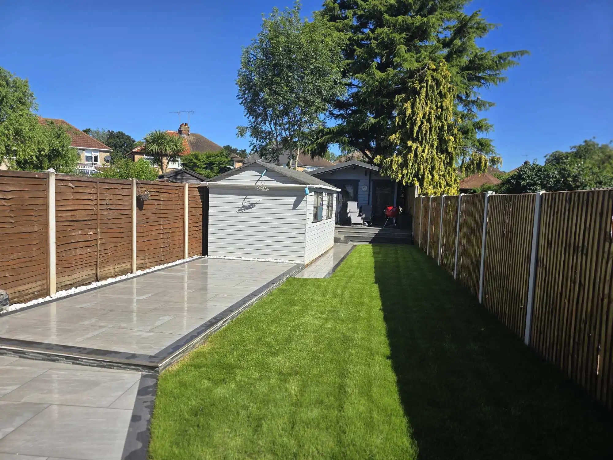 Silver patio beside a white outbuilding and lawn