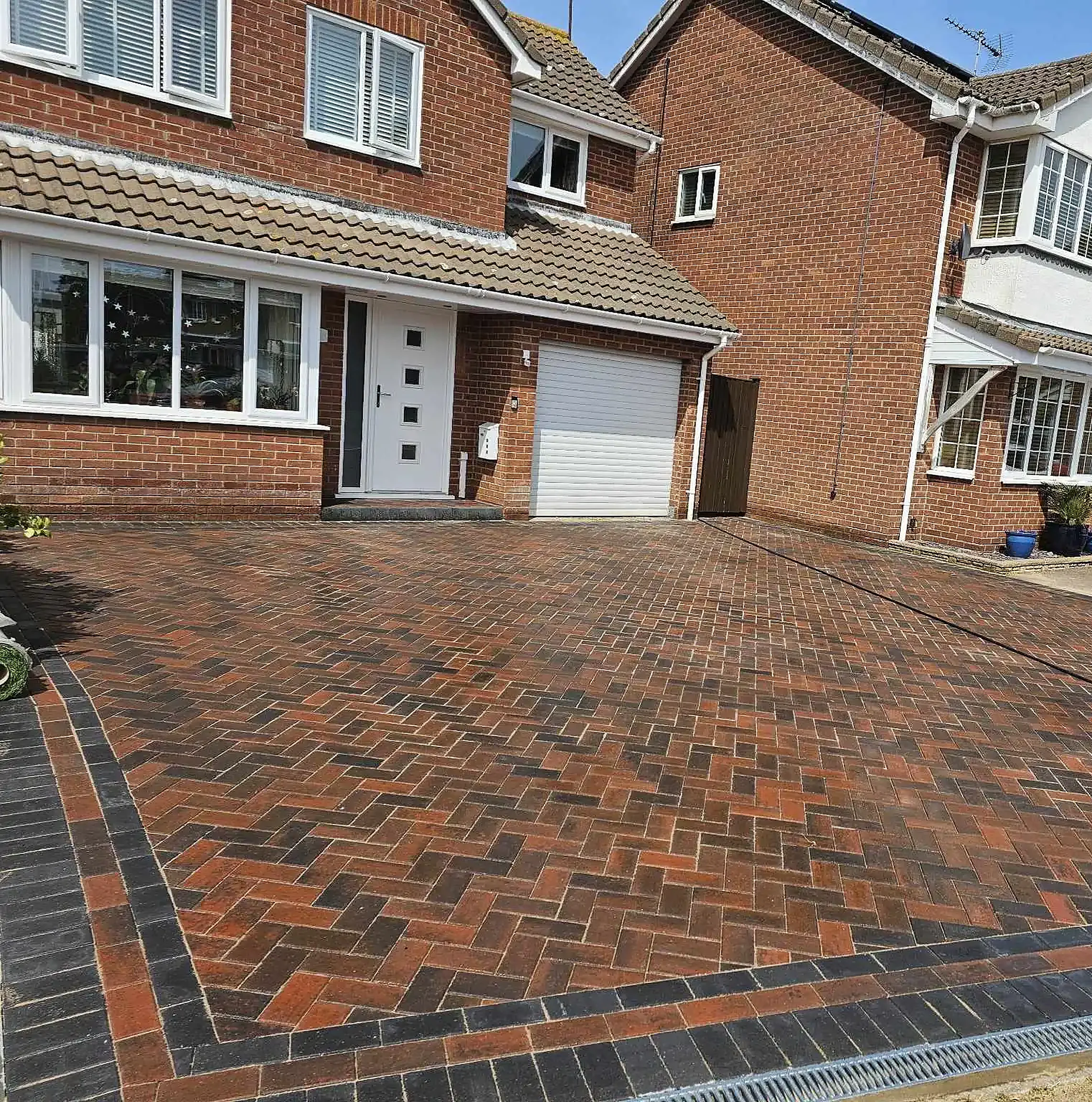 Red herringbone block paved driveway with a charcoal border at a brick house